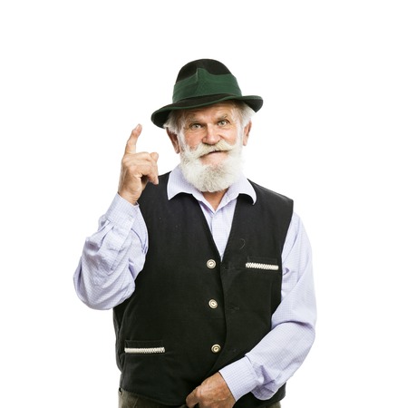 Portrait of old bearded bavarian man in traditional hat pointing upwards isolated on white backgroundの写真素材