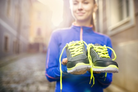 Young female runner carrying her running shoes in old city centerの写真素材