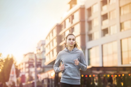 Young female runner in hoody is jogging in the city streetの写真素材