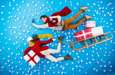 Happy young couple on sledge with Christmas presents against the blue background with snowflakesの写真素材