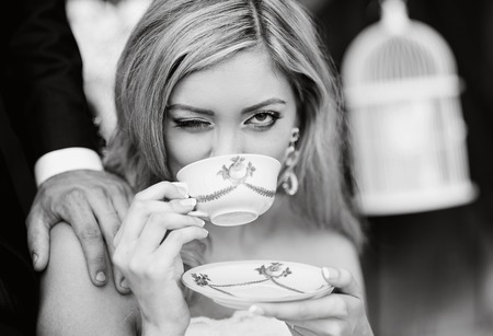 Bride drinking coffee from vintage cup and sitting by the old houseの写真素材