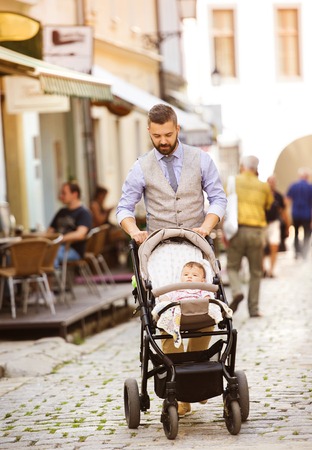 Handsome hipster modern businessman with beard walking with baby in pram in townの写真素材