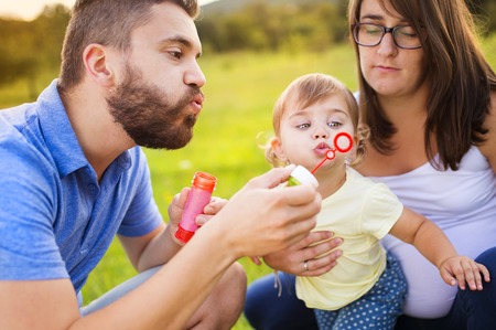 Happy little girl with her parents blowing bubbles in summer natureの写真素材
