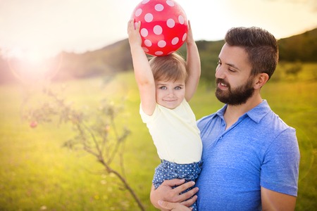 Smiling father and his little daughter playing with ball in summer nature.の写真素材