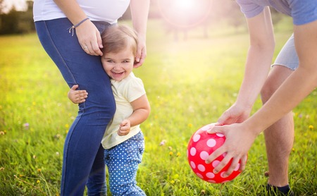 Happy pregnant family with little girl having fun playing with ball in summer natureの写真素材