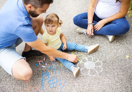 Close up of little girl and her parents drawing with chalks on the sidewalkの写真素材