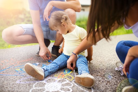 Close up of little girl and her parents drawing with chalks on the sidewalkの写真素材