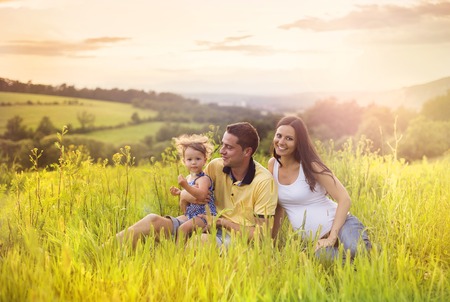 Happy pregnant family with little daughter spending time together sitting in grass in summer natureの写真素材