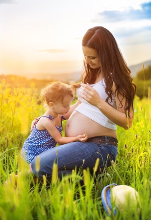Cute little girl touching her mother\'s pregnant belly in summer natureの写真素材