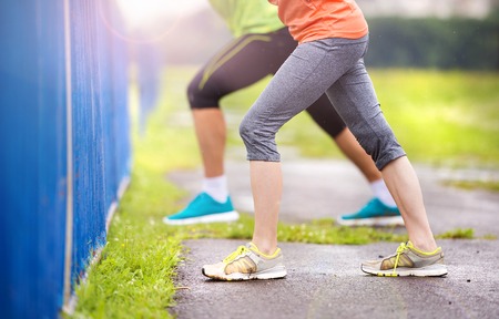 Young couple stretching after the run on asphalt in rainy weather. Details of legs.