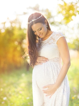 Outdoor natural portrait of beautiful pregnant woman in white dressの写真素材