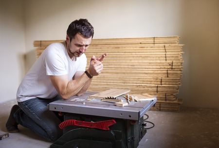 Young handyman having accident during cutting plywood on circular sawの写真素材
