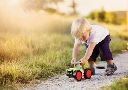 Little boy playing with toy tractor on countryside roadの写真素材