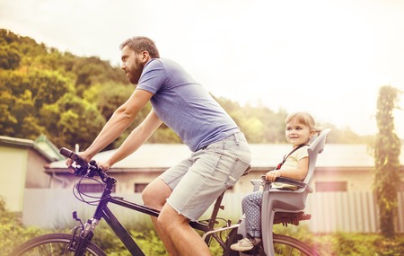 Young father with his little daughter on bicycle in green sunny parkの写真素材