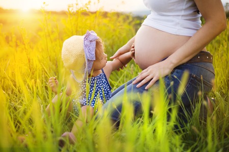 Cute little girl touching her mother\'s pregnant belly in summer natureの写真素材