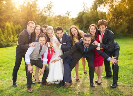 Full length portrait of newlywed couple having fun with bridesmaids and groomsmen in green sunny parkの写真素材