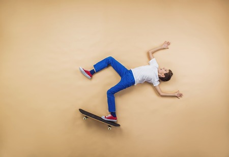 Funny boy is playing with skateboard. Lying on the floor.