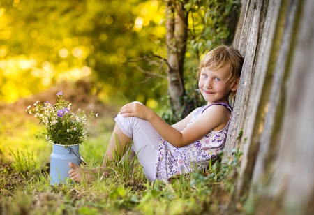 Little blonde girl holding meadow flowers laughing by the wooden fenceの写真素材