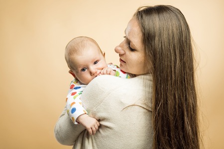Mother holding a baby tenderly in her arms studio shot on beige backgroundの写真素材
