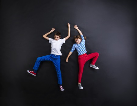 Playful young siblings laughing and having fun together. Studio shot on a black background.の写真素材