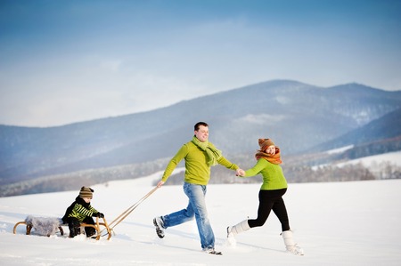 Happy parents with their son riding on sledge having fun outside in the snow.の写真素材