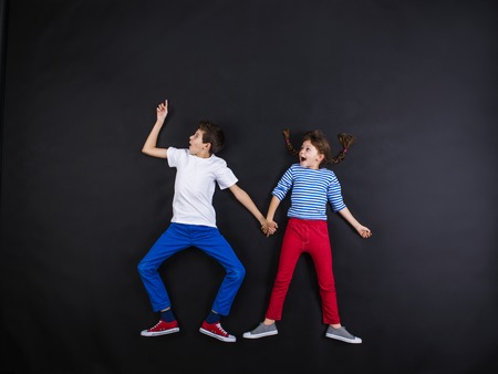 Playful young siblings laughing and having fun together. Studio shot on a black background.の写真素材