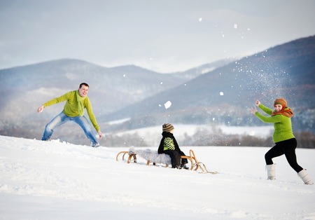 Happy parents with their son riding on sledge having fun outside in the snow.