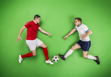 Two football players fighting for a ball. Studio shot on a green backgroud.の写真素材