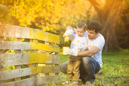 Cute little boy and his father painting wooden fence together on sunny day in natureの写真素材