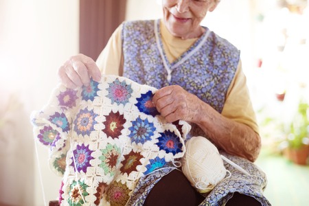 Old woman is knitting a blanket inside in her living roomの写真素材