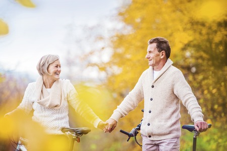 Active seniors riding bikes in autumn nature. They having romantic time outdoor.の写真素材