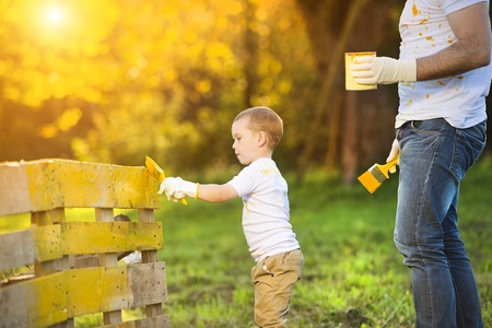 Cute little boy and his father painting wooden fence together on sunny day in natureの写真素材