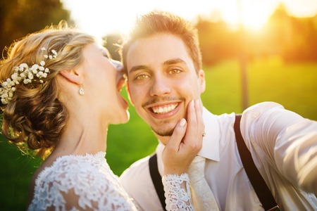 Young wedding couple taking a selfie of themselves as they enjoy romantic moments outside on a summer meadowの写真素材