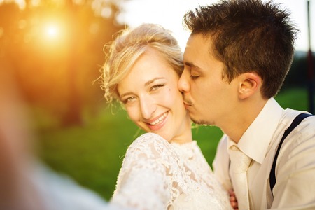 Young wedding couple taking a selfie of themselves as they enjoy romantic moments outside on a summer meadowの写真素材