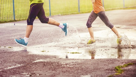 Young couple jogging on asphalt in rainy weatherの写真素材