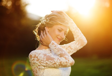 Happy beautiful young bride outside on a summer meadow at the sunsetの写真素材