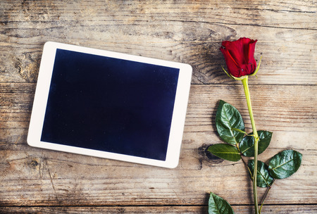 Valentine´s day composition of yet not written love message in a tablet and a red rose. Studio shot on a wooden floor backround.の写真素材