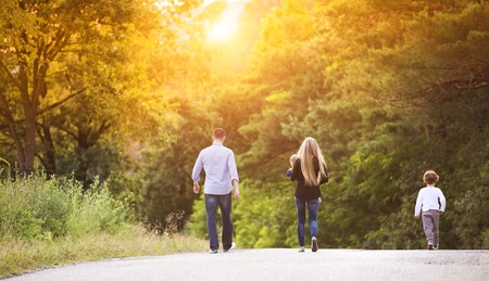Happy young family walking down the road outside in green nature.の写真素材