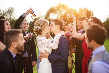 Full length portrait of newlywed couple and their friends at the wedding party showered with confetti in green sunny parkの写真素材