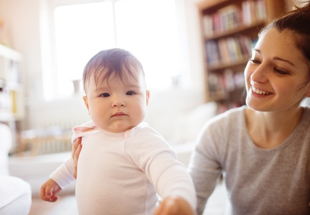 Cute little baby girl playing with her mother on a carpet in a living room.の写真素材