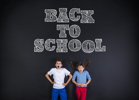 Cute boy and girl standing in frot of a big blackboard. Studio shot on black background.の写真素材