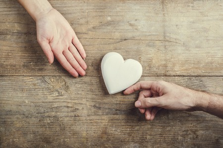 Man offering a white heart tenderly to a woman. Studio shot on a wooden background, view from above.の写真素材