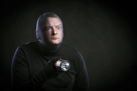 Thief in action with balaclava on his face, dressed in black. Studio shot on black background.の写真素材