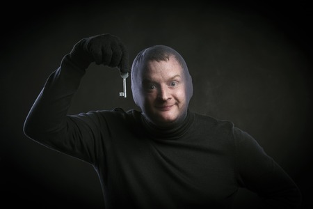 Thief in action with balaclava on his face, dressed in black. Studio shot on black background.の写真素材