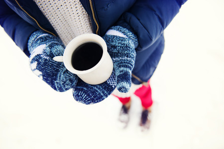 Hands of young woman holding a cup of coffee outside in snowの写真素材