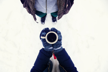 Hands of young woman holding a cup of coffee outside in snow