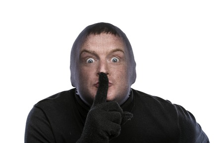 Thief in balaclava making funny faces, dressed in black. Studio shot on white background.の写真素材