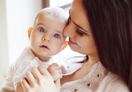 Cute little baby in the arms of her mother in a living room.の写真素材