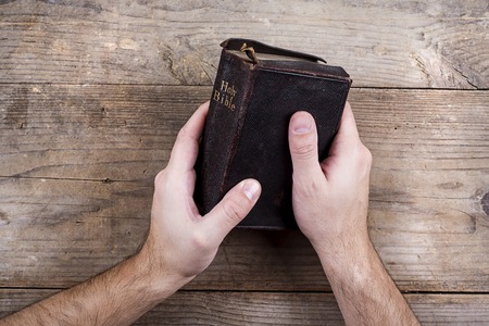 Hands holding Bible on a wooden desk background.の写真素材