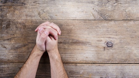 Hands of praying young man on a wooden desk background.の写真素材